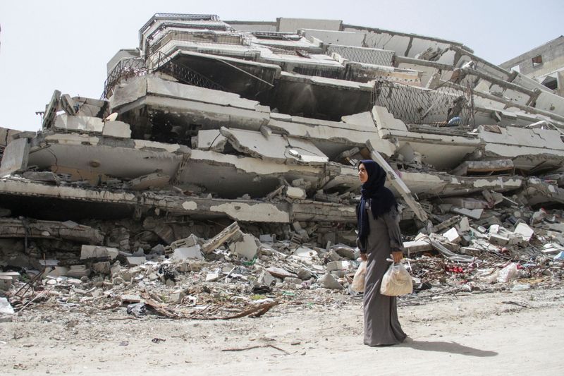 &copy; Reuters. FILE PHOTO: Palestinian woman Asmaa Al-Belbasi, making her way back to her shelter after buying bread from recently reopened Al-Sharq bakery, walks past the ruins of a house destroyed during Israel's military offensive, amid the ongoing conflict between I
