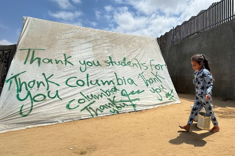 © Reuters. FILE PHOTO: A girl walks next to a tent sprayed with a message in solidarity with pro-Palestinian university students, amid the ongoing conflict between Israel and Palestinians, in Rafah in the southern Gaza Strip, May 2, 2024. REUTERS/Mohammed Salem/File Photo
