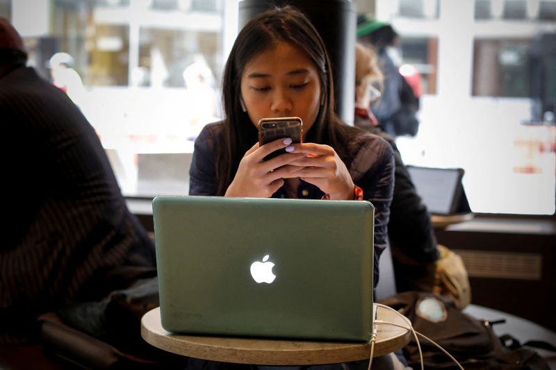 © Reuters. FILE PHOTO: A woman uses her Apple iPhone and laptop in a cafe in lower Manhattan in New York City, U.S., May 8, 2019. REUTERS/Mike Segar/File Photo