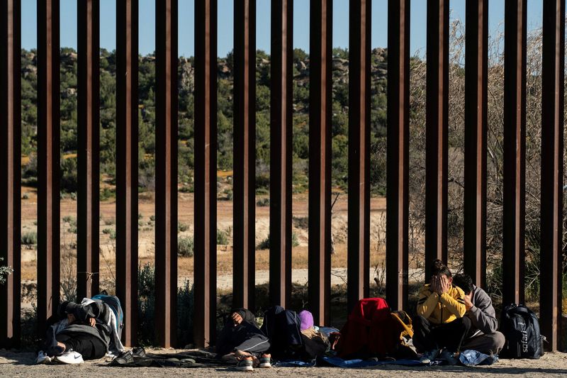 &copy; Reuters. FILE PHOTO: Asylum-seeking migrants from India wait by the border wall while waiting to be picked up by the U.S. Border Patrol after crossing the border from Mexico into the U.S. in Jacumba Hot Springs, California, U.S. April 27, 2024.  REUTERS/Go Nakamur