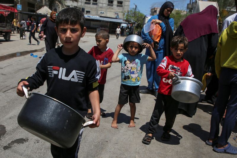 &copy; Reuters. Niños palestinos cargados con ollas esperan para recibir alimentos cocinados por una cocina de caridad, en medio de la escasez de suministros de ayuda, después de que las fuerzas israelíes lanzaran una operación terrestre y aérea en la parte oriental