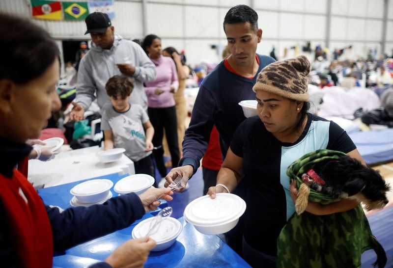 &copy; Reuters. Refugiados venezuelanos Carina Gonzales e Xavier Velasquez recebem comida de um voluntário em abrigo em Porto Alegre depois que a casa onde viviam foi destruída pelas enchentes no Estado.
REUTERS/Adriano Machado