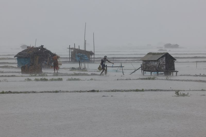 © Reuters. People walk along shrimp and crab farms that are flooded due to heavy rain as Cyclone Remal passes the country, in the Shyamnagar area of Satkhira, Bangladesh, May 27, 2024. REUTERS/Mohammad Ponir Hossain     