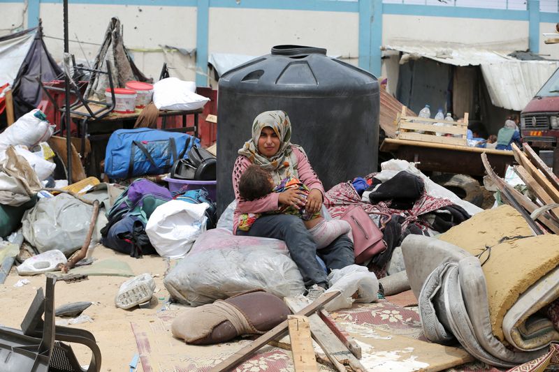 © Reuters. A woman sits with a child, on the day Palestinians travel on foot along with their belongings, as they flee Rafah due to an Israeli military operation, in Rafah, in the southern Gaza Strip, May 28, 2024. REUTERS/Hatem Khaled