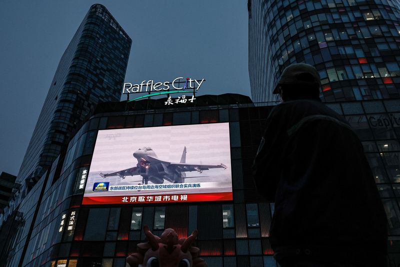 © Reuters. A man looks at a giant screen showing news footage of military drills conducted in areas around the island of Taiwan by the Eastern Theatre Command of the Chinese People's Liberation Army (PLA), in Beijing, China May 24, 2024. REUTERS/Tingshu Wang