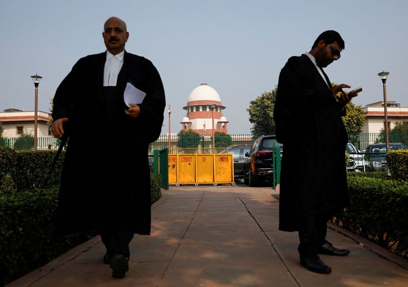 © Reuters. FILE PHOTO: A lawyer looks into his mobile phone as another walks past, in front of India's Supreme Court in New Delhi, December 11, 2023. REUTERS/Adnan Abidi/File Photo