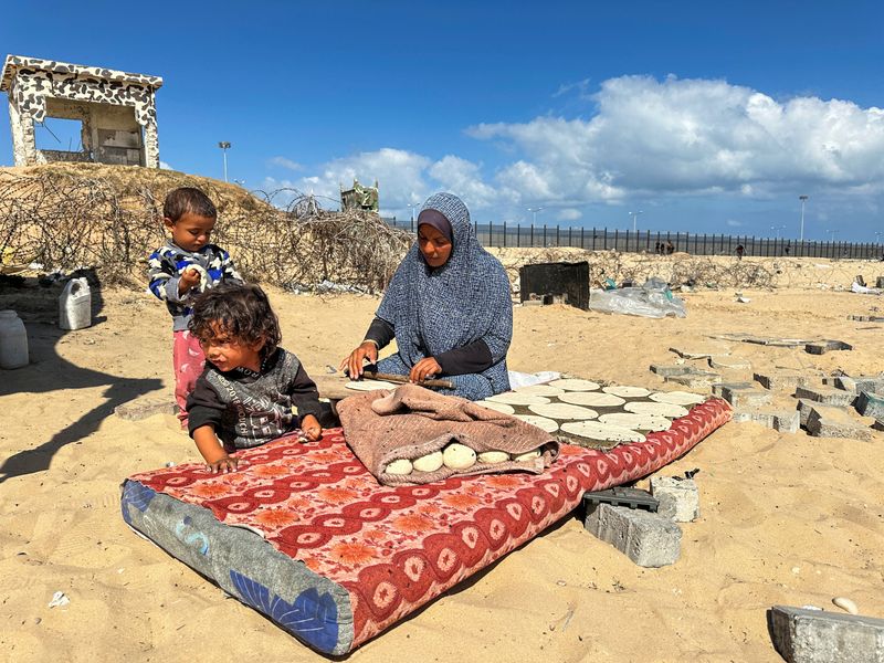 © Reuters. FILE PHOTO: A woman prepares food next to children, as displaced Palestinians take shelter at the border with Egypt, during an Israeli military operation, in Rafah in the southern Gaza Strip, May 29, 2024. REUTERS/Doaa Rouqa/File Photo