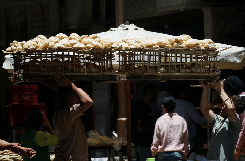 © Reuters. FILE PHOTO: An Egyptian man is helped by another person, as he carries bread on a wooden rack to be sold to customers after the price of subsidised bread jumped 300% to 20 piasters ($0.0042) from 5 piasters in Cairo, Egypt June 3, 2024. REUTERS/Amr Abdallah Dalsh/File Photo