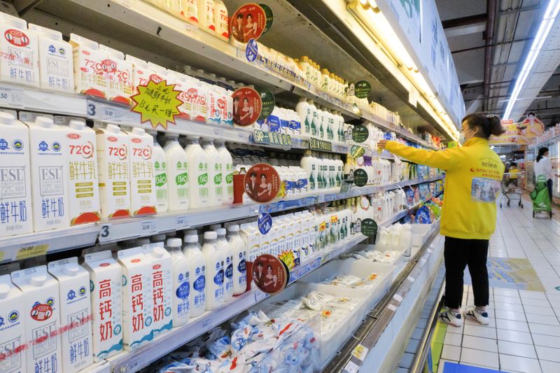 © Reuters. FILE PHOTO: A staff member arranges cartons of milk on refrigerator shelves at a supermarket in Beijing, China, May 21, 2021. Picture taken May 21, 2021. REUTERS/Thomas Peter/File Photo