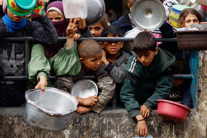 © Reuters. Palestinian children wait to receive food cooked by a charity kitchen amid shortages of food supplies, as the ongoing conflict between Israel and the Palestinian Islamist group Hamas continues, in Rafah, in the southern Gaza Strip, February 13, 2024. REUTERS/Ibraheem Abu Mustafa