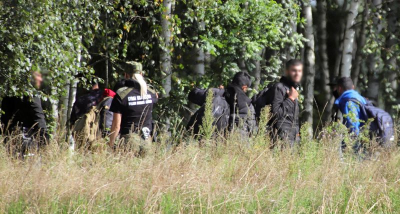 © Reuters. FILE PHOTO: A Polish border patrol officer is seen next to a group of migrants stranded on the border between Belarus and Poland near the village of Usnarz Gorny, Poland August 22, 2021. Grzegorz Dabrowski/Agencja Gazeta/via REUTERS/File photo