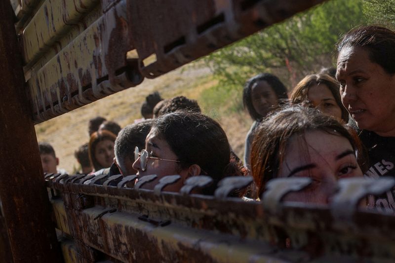 © Reuters. FILE PHOTO: Migrants from South and Central America look towards the United States through a gap in the border wall before crossing into Boulevard, California as they line up to enter the United States from Tecate, Mexico, May 20, 2024. REUTERS/Adrees Latif/File Photo