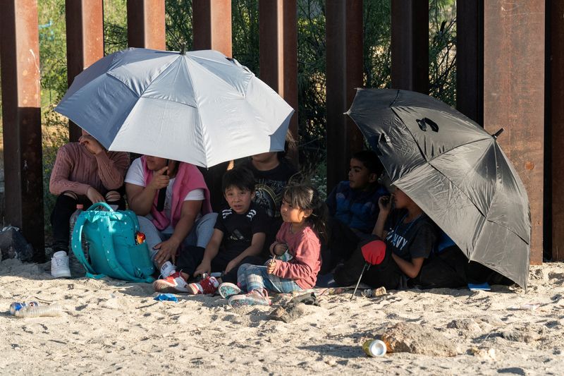 © Reuters. FILE PHOTO: Asylum-seeking migrants from Mexico use umbrellas to stay under shade while waiting at the border wall to be transported, after U.S. President Joe Biden announced a sweeping border security enforcement effort, in Jacumba Hot Springs, California, U.S. June 4, 2024.  REUTERS/Go Nakamura/File Photo