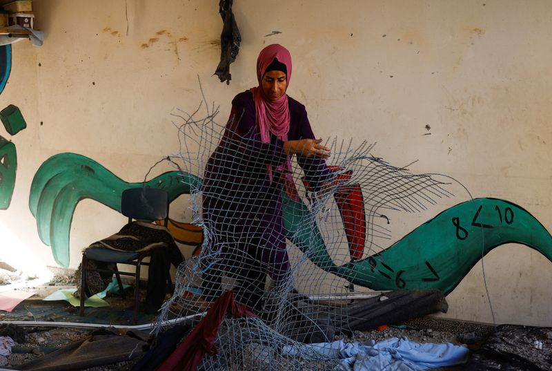 © Reuters.  A Palestinian woman repairs a classroom at the UNRWA school where she lives, after an air strike on a house neighboring the school in Khan Younis, in the southern Gaza Strip, June 21, 2024. REUTERS/Mohammed Salem