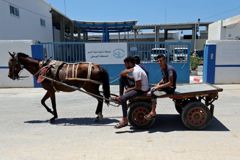 © Reuters. FILE PHOTO: Palestinians ride a horse-drawn cart past Gaza desalination plant, in the central Gaza Strip June 23, 2019. REUTERS/Ibraheem Abu Mustafa/File Photo