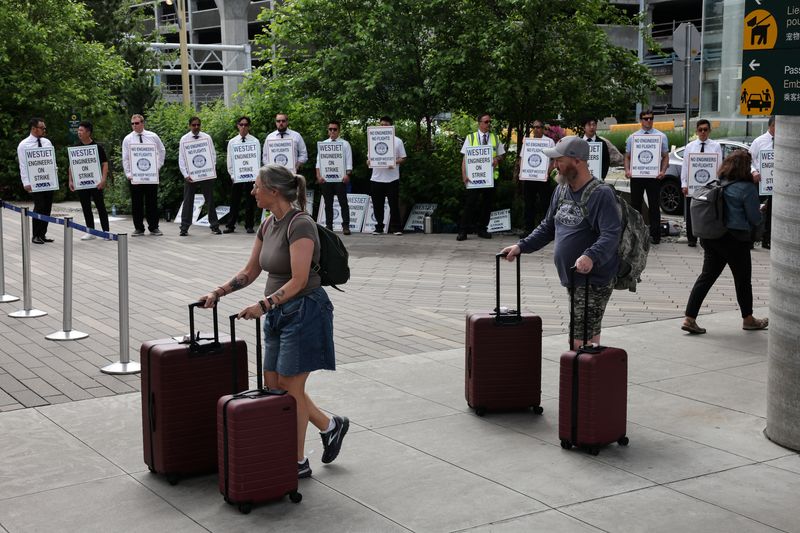 &copy; Reuters. People walk with their luggage as striking aircraft maintenance engineers and technical staff represented by the Aircraft Mechanics Fraternal Association union stand in a picket line against Westjet Airlines at Vancouver International Airport in Richmond,