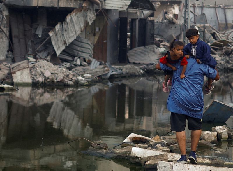 &copy; Reuters. FILE PHOTO: A Palestinian man holds his children as he walks next to buildings destroyed in an Israeli strike, amid the ongoing conflict between Israel and Hamas, in Khan Younis, in the southern Gaza Strip, June 30, 2024. REUTERS/Mohammed Salem/File Photo