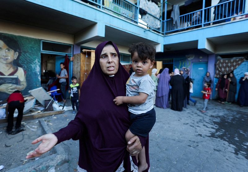 © Reuters. A Palestinian woman carrying a child reacts, after an Israeli air strike on a UN school sheltering displaced people, amid the Israel-Hamas conflict, in Nusairat in central Gaza Strip, July 6, 2024. REUTERS/Ramadan Abed 