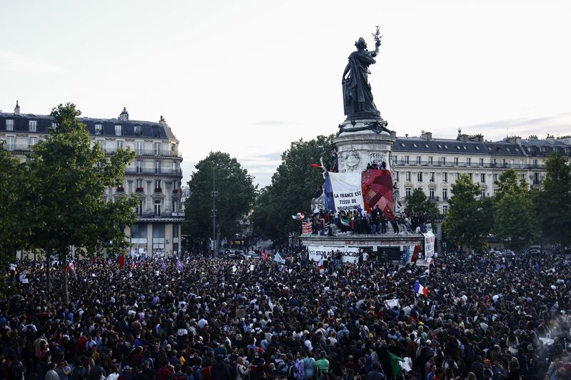 © Reuters. Protesters hold a giant French flag on the statue of Marianne as people gather at the Place de la Republique after partial results in the second round of the early French parliamentary elections, in Paris, France, July 7, 2024. REUTERS/Yara Nardi