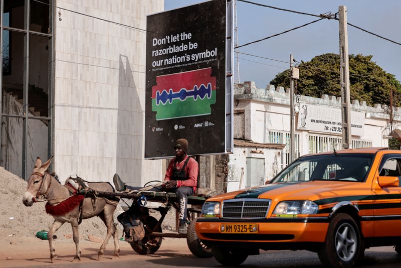 © Reuters. A man rides a cart past a poster advocating for an end to female genital mutilation (FGM), in Banjul, Gambia, June 6, 2024. REUTERS/Zohra Bensemra