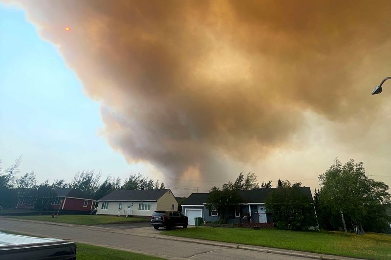 © Reuters. Smoke from an encroaching wildfire is seen over homes after an evacuation was ordered in the eastern Canadian community of Labrador City, Newfoundland, Canada July 12, 2024.  REUTERS/Josh Bingle