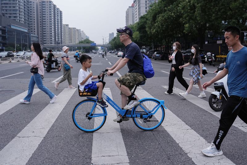 © Reuters. A person rides a bicycle with a child sitting in the basket in Beijing, China July 14, 2024. REUTERS/Tingshu Wang