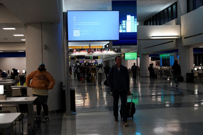 © Reuters. FILE PHOTO: Travelers walk past a monitor displaying a blue error screen, also known as the 