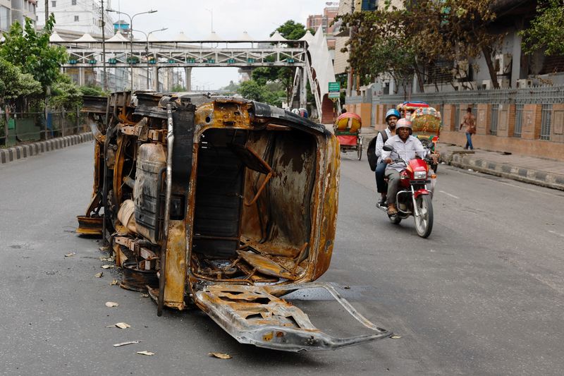 &copy; Reuters. Men ride on a motorbike past a damaged vehicle that was set afire by a mob during clashes after violence erupted following protests by students against government job quotas, in Dhaka, Bangladesh, July 22, 2024. REUTERS/Mohammad Ponir Hossain/ File Photo