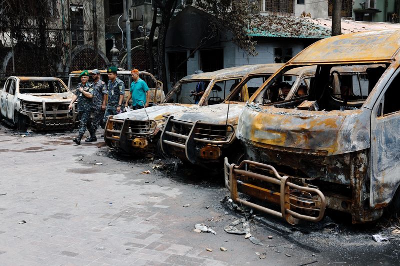 © Reuters. Security personnel walk past damaged vehicles of a government owned organization, that were set afire by a mob during clashes after violence erupted following protests by students against government job quotas, in Dhaka, Bangladesh, July 22, 2024. REUTERS/Mohammad Ponir Hossain