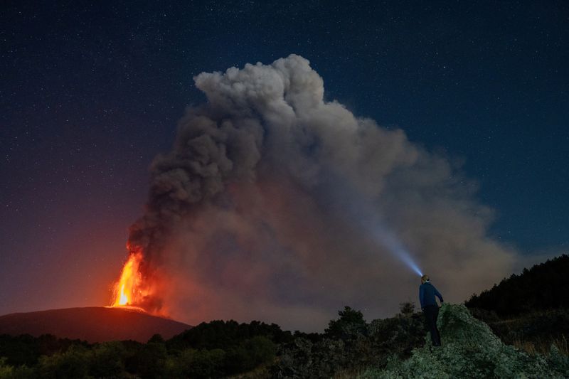 &copy; Reuters. Una persona osserva la lava e i pennacchi di fumo che si levano da un cratere dell'Etna, il vulcano più attivo d'Europa, Italia, 15 luglio 2024. REUTERS/Camminata dell'Etna/Giuseppe Di Stefano/fotogramma