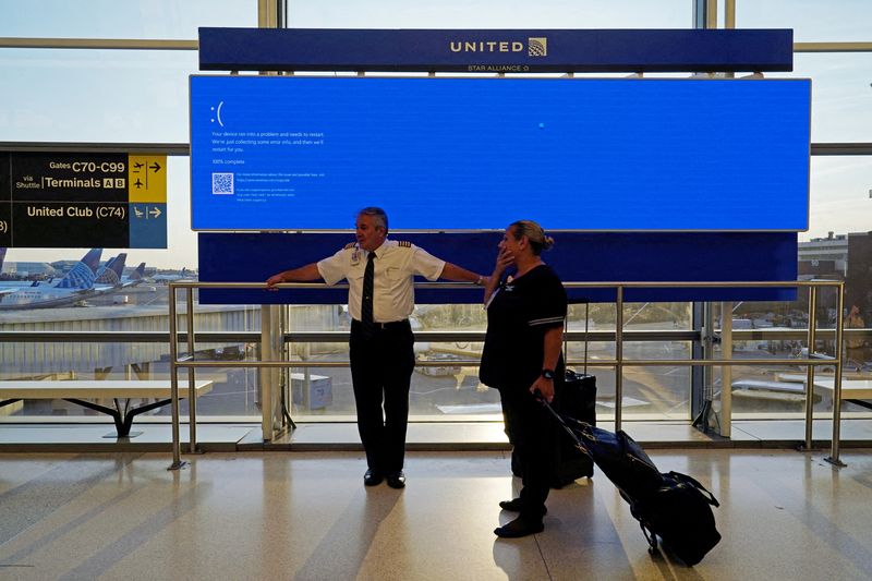 © Reuters. FILE PHOTO: United Airlines employees wait by a departures monitor displaying a blue error screen, also known as the “Blue Screen of Death” inside Terminal C in Newark International Airport, after United Airlines and other airlines grounded flights due to a worldwide tech outage caused by an update to CrowdStrike's 