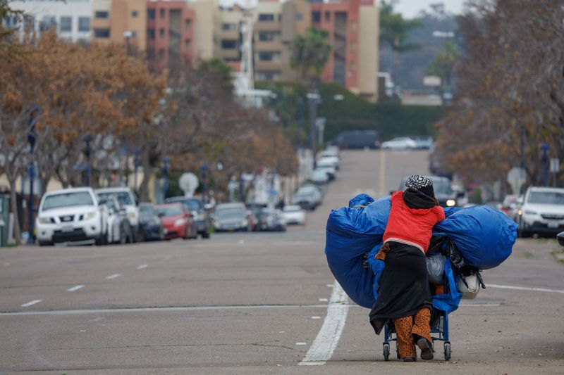 © Reuters. FILE PHOTO: A homeless women moves her belongings to the side of a freeway on land under state jurisdiction, after being evicted from a location along a downtown street by police, in San Diego, California, U.S., February 26, 2024.  REUTERS/Mike Blake