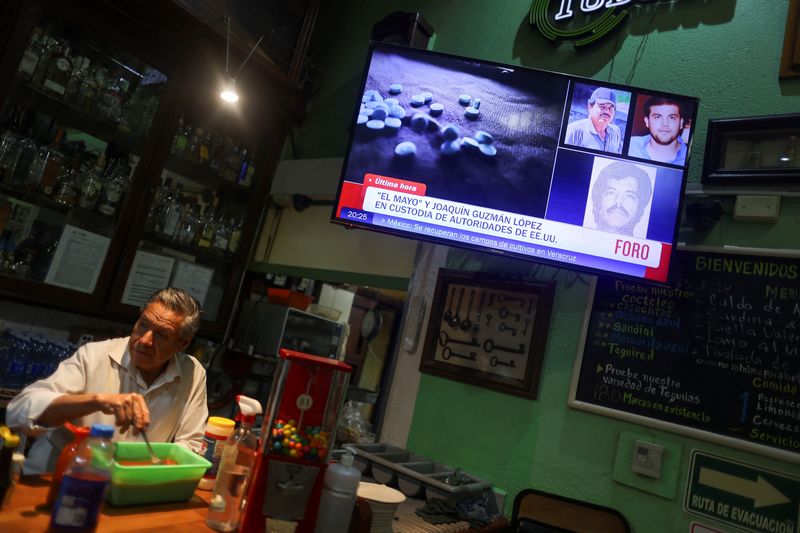 © Reuters. A barman stands next to a TV showing the news of the arrest of Mexican drug lord Ismael 