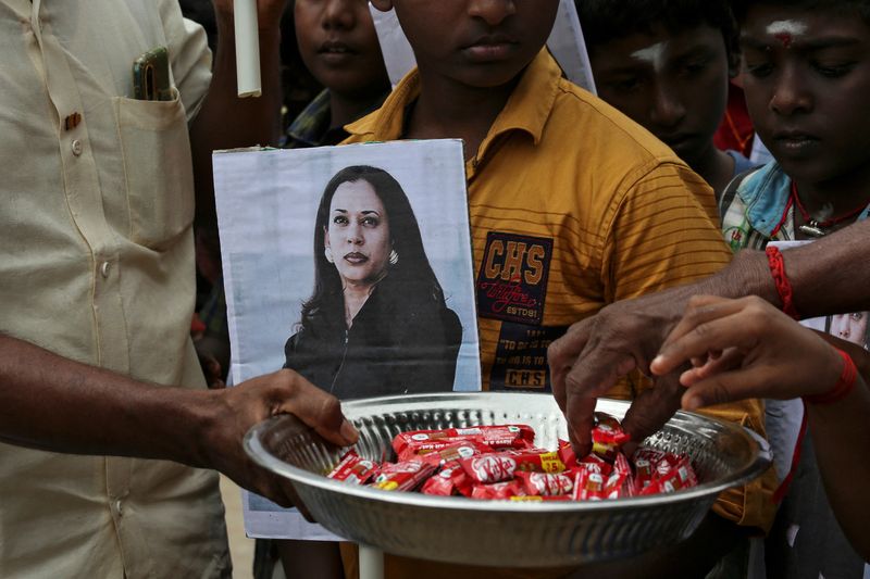 © Reuters. FILE PHOTO: A man holds a placard with the photo of U.S. Vice President-elect Kamala Harris as another distributes sweets during the celebration on the day of her inauguration, in the village of Thulasendrapuram, where Harris' maternal grandfather was born and grew up, in the southern Indian state of Tamil Nadu, India, January 20, 2021. REUTERS/P. Ravikumar/File Photo