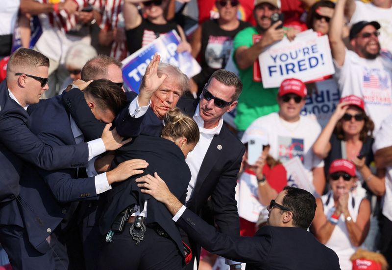 © Reuters. FILE PHOTO: Republican presidential candidate and former U.S. President Donald Trump gestures with a bloodied face while he is assisted by U.S. Secret Service personnel after he was shot in the right ear during a campaign rally at the Butler Farm Show in Butler, Pennsylvania, U.S., July 13, 2024. REUTERS/Brendan McDermid/File Photo