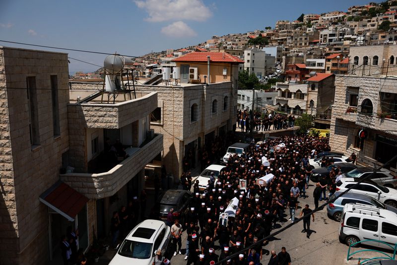 © Reuters. Mourners carry coffins, during the funeral of children who were killed at a soccer pitch by a rocket Israel says was fired from Lebanon, in Majdal Shams, a Druze village in the Israeli-occupied Golan Heights, July 28, 2024. REUTERS/Ammar Awad