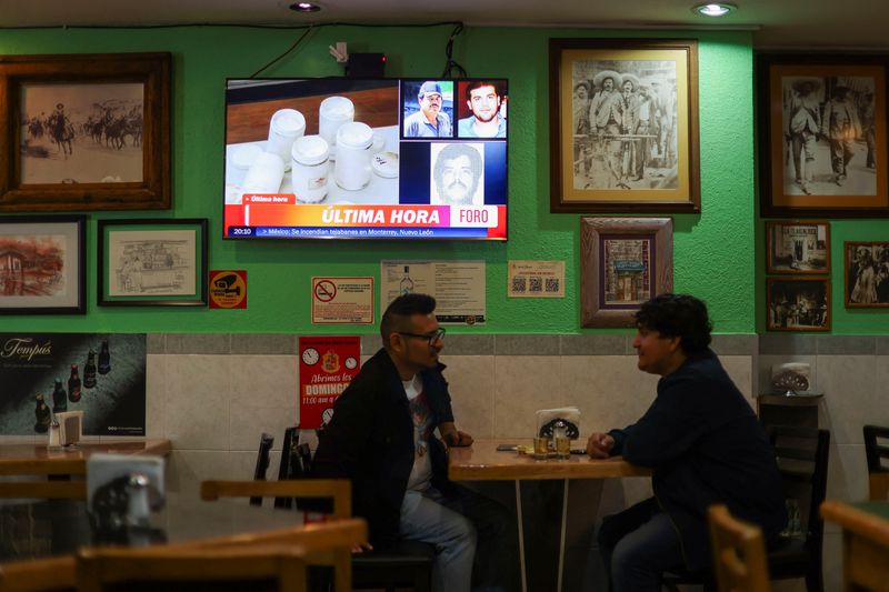 © Reuters. Patrons talk and drink next to a TV showing the news of the arrest of Mexican drug lord Ismael 