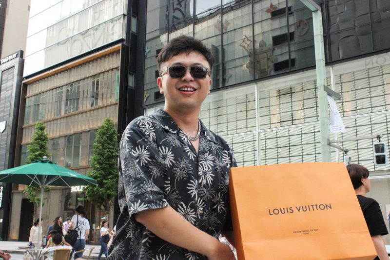 © Reuters. Chinese tourist Zhang Lei poses with a recent purchase in the Ginza shopping district of Tokyo, Japan, July 27, 2024. REUTERS/David Dolan