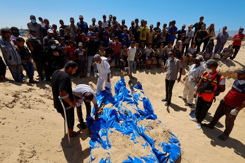 © Reuters. People watch as the bodies of unidentified Palestinians are buried at a mass grave after the bodies were handed over by Israel, amid Israel-Hamas conflict, in Khan Younis, in the southern Gaza Strip August 5, 2024. REUTERS/Mohammed Salem