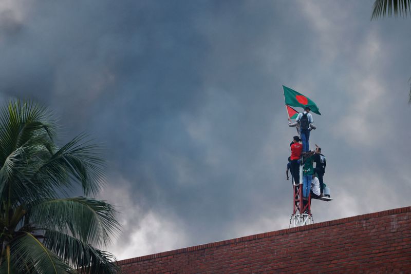 © Reuters. People wave a Bangladesh flag as they climb a structure at Ganabhaban, the Prime Minister's residence, after the resignation of the Sheikh Hasina in Dhaka, Bangladesh, August 5, 2024. REUTERS/Mohammad Ponir Hossain