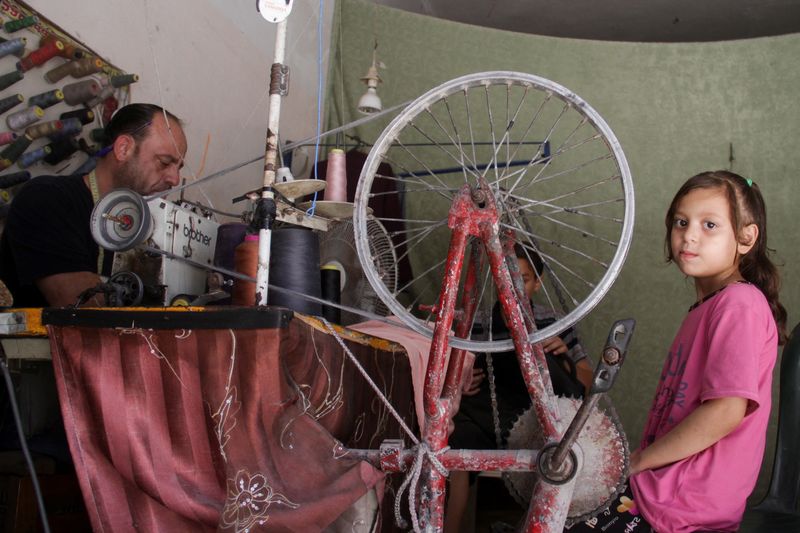 © Reuters. Palestinian tailor Raad Saad powers his sewing machine with a bicycle and help from his children, amid power cut, as conflict between Israel and Hamas continues, in the northern Gaza Strip July 30, 2024. REUTERS/Mahmoud Issa