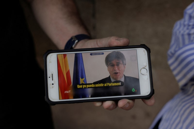 © Reuters. A journalist holds a mobile phone as he watches self-exiled former Catalan pro-independence leader Carles Puigdemont announcing that he has undertaken the return journey from exile to Spain, to attend to the investiture debate of Catalonia, near the Catalonia Regional Parliament, a day before the investiture debate of Catalonia to elect a new leader, in Barcelona, Spain, August 7, 2024. REUTERS/Jon Nazca 