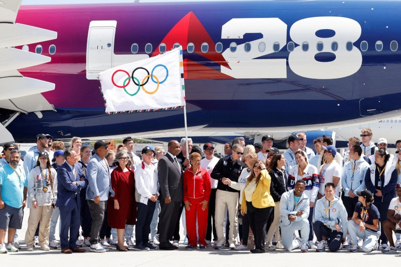 © Reuters. Members of LA28, local government officials and U.S. olympic athletes pose with the official Olympic flag as it returns to Los Angeles for the first time in 40 years, in Los Angeles, California, U.S. August 12, 2024. REUTERS/Carlin Stiehl