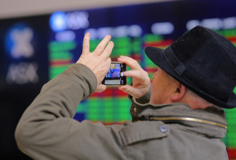 © Reuters. FILE PHOTO: An investor takes a photograph using his phone as he stands in front a board displaying stock prices at the Australian Securities Exchange (ASX) in Sydney, Australia, July 17, 2017. REUTERS/Steven Saphore/File Photo