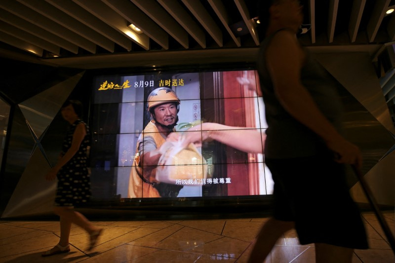 © Reuters. People walk past a screen showing a movie trailer for the Chinese film 