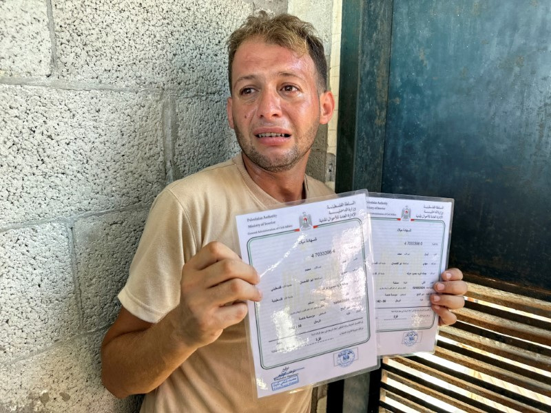 © Reuters. Mohammed Abu Al-Qumsan, whose wife Jumann, and newborn twins Asser and Ayssel were killed in an Israeli strike while he was bringing the twins' birth certificates, according to medics, reacts as he holds the certificates, in Deir Al-Balah in the central Gaza Strip, August 13, 2024. REUTERS/Abdullah Al-Attar     