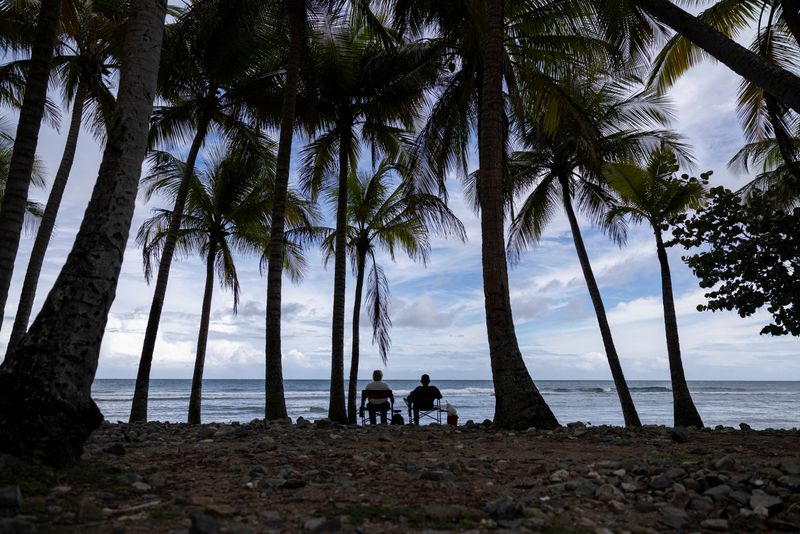 © Reuters. A couple sits in front of the sea at Inches Beach as Tropical Storm Ernesto approaches, in Patillas, Puerto Rico August 13, 2024.  REUTERS/Ricardo Arduengo