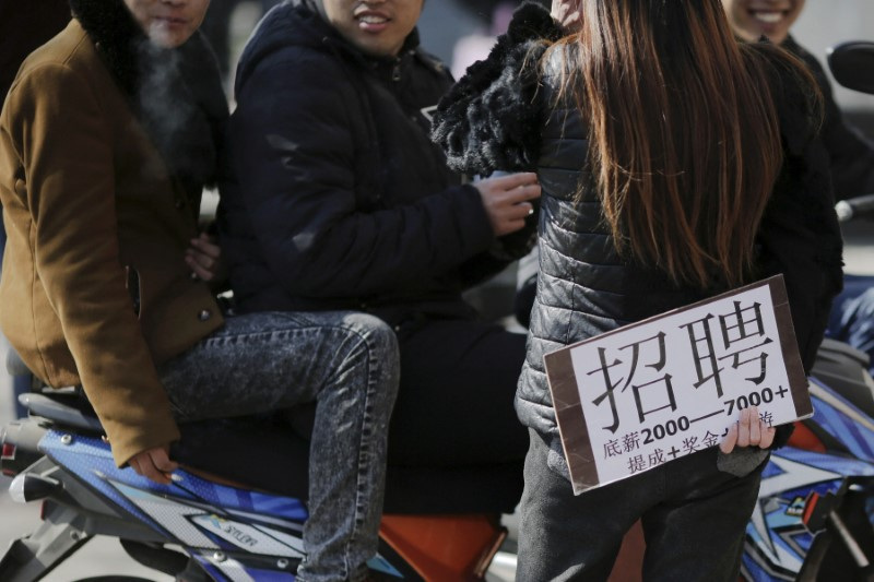 © Reuters. FILE PHOTO: A recruiter holding a placard advertising jobs talks to young men at an unofficial job market in suburbs of Beijing, China February 24, 2016.  REUTERS/Damir Sagolj/File Photo