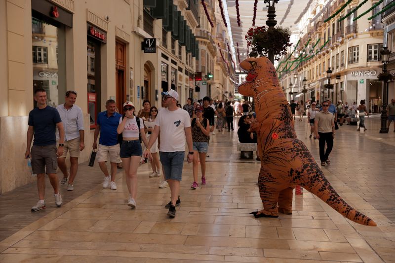 &copy; Reuters. Tourists walk past a man in a dinosaur costume at Larios Street, on a hot summer day, in downtown Malaga, Spain, August 14, 2024. REUTERS/Jon Nazca