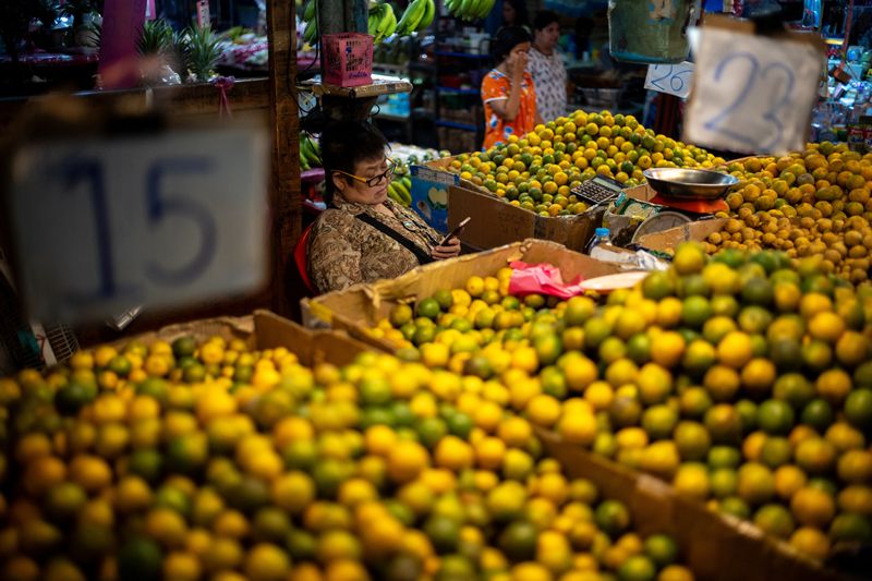 © Reuters. FILE PHOTO: A vendor looks at a mobile phone at her fruit stall at a market in Bangkok, Thailand October 2, 2023. REUTERS/Athit Perawongmetha/File Photo